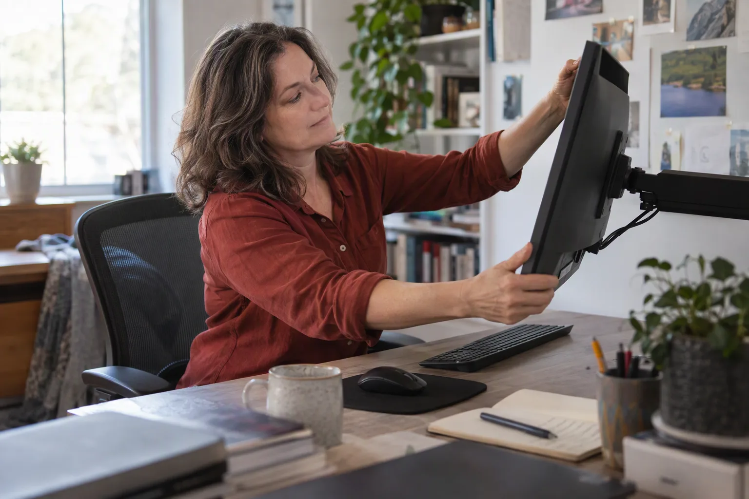 A professional adjusts a monitor at a lived-in workstation with separate input devices.